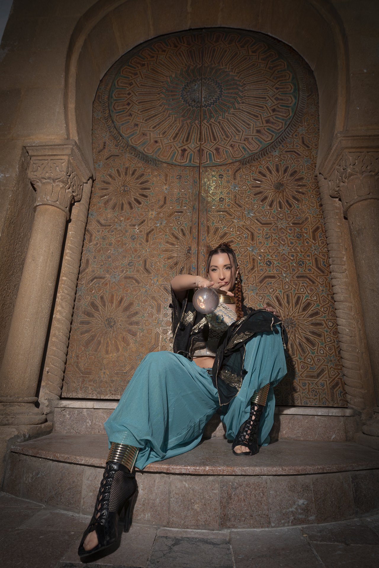 Sereia seated with crystal contact ball in front of an ornate carved door